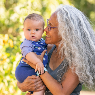 A smiling woman holding her infant grandchild knowing her financial legacy is protected.