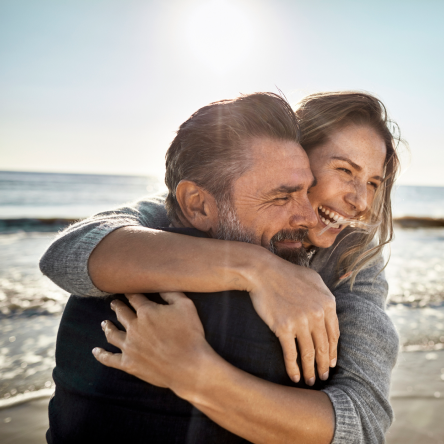 Financial clients happily embrace on a sunny day at the beach after choosing the ideal life insurance to suit their needs.