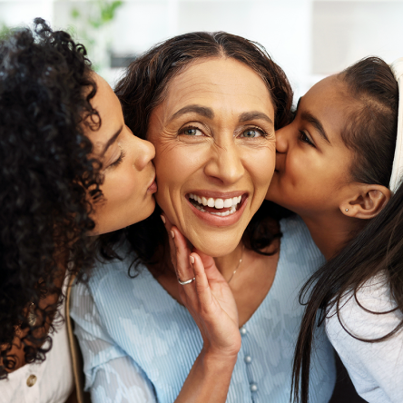 A mother being kissed on the cheeks by her daughters.