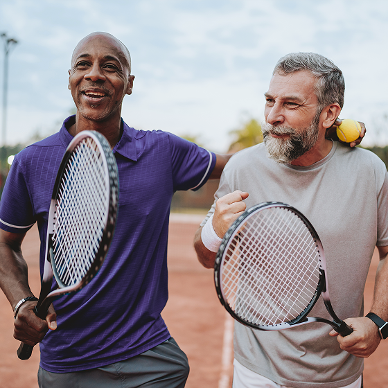 Two men holding tennis rackets celebrate their win on the court.