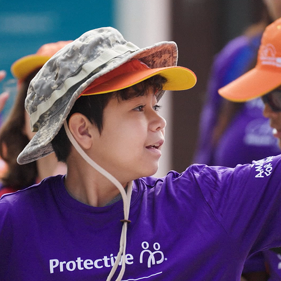 Kid wearing a Protective tee shirt practices his serve at the Amigos for Kids tennis clinic.