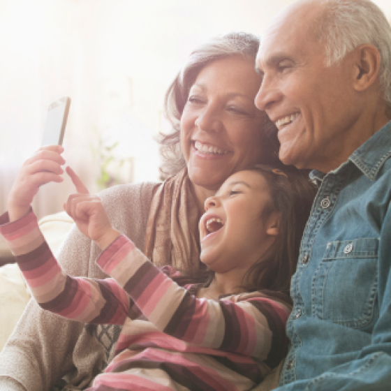 An older couple and grandchild laughing at content on a mobile phone.