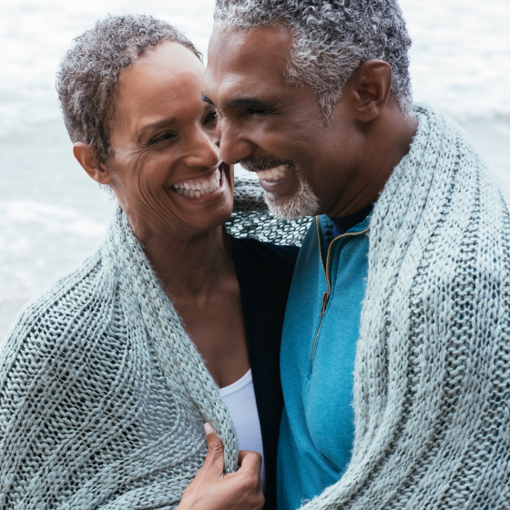 Couple laugh as they try to share a shawl to protect themselves from a cold breeze.