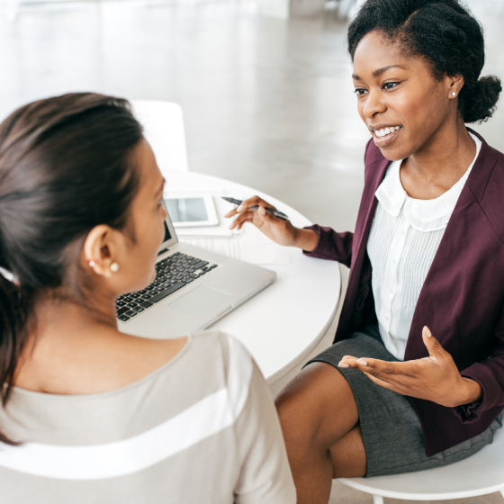 A financial professional talking to a client at a table, with a laptop.
