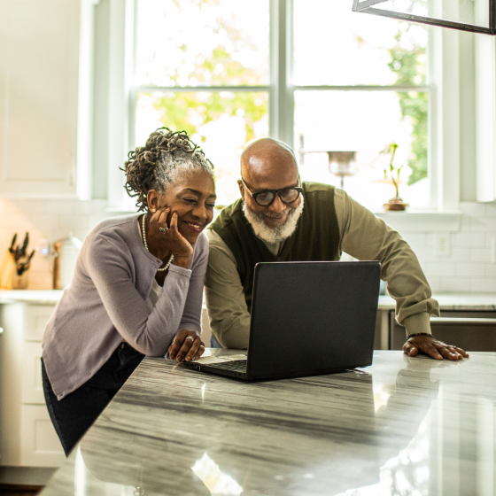 Smiling couple in front of a computer, reading about the SecurePay 5 benefit and how it can help safeguard their retirement income.