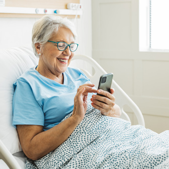 A woman using her smartphone in a hospital bed, reading about her terminal illness benefits.