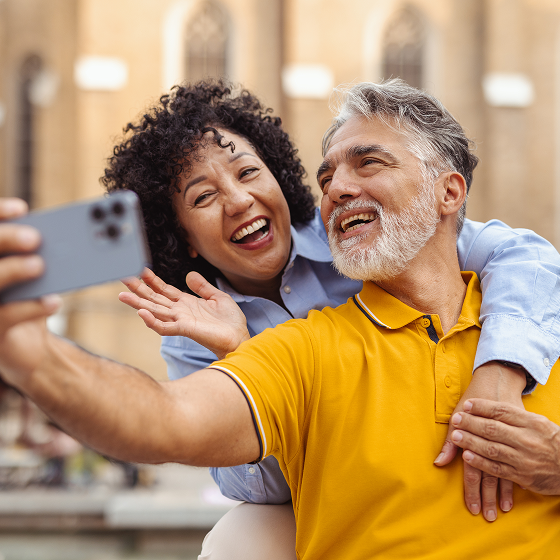A happy older couple laughs while taking a selfie outdoors.