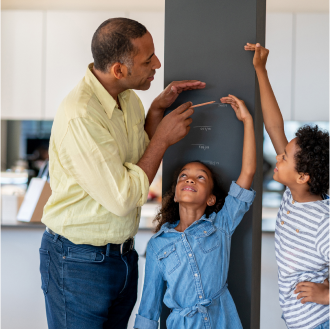 A father helping his children measure their growth, knowing his family is protected with variable universal life insurance.
